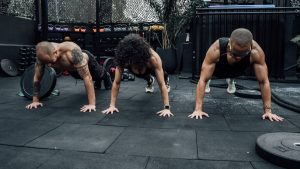 Three individuals performing push-ups together in a Mexico City gym setting.